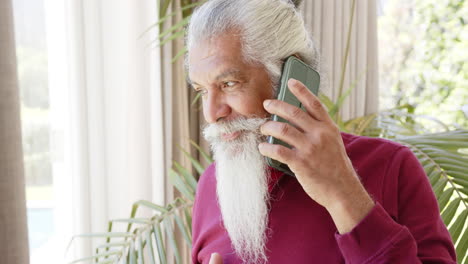 Happy-biracial-senior-man-with-white-beard-on-smartphone-in-sunny-room,-copy-space,-slow-motion