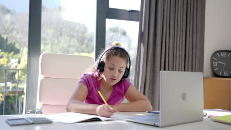Chica-Birracial-Feliz-Usando-Auriculares-Y-Computadora-Portátil-Para-Clases-Escolares-En-Línea-En-Casa