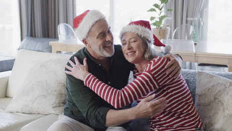 Middle-aged-caucasian-couple-in-santa-hats-cuddling-at-christmas-at-home,-slow-motion