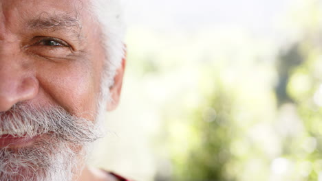 Half-portrait-of-biracial-man-with-white-beard-smiling-in-sunny-nature,-copy-space,-slow-motion