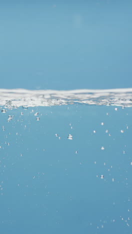 Vertical-video-of-beauty-product-bottle-falling-in-water-with-copy-space-on-blue-background