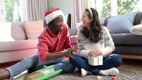 Happy-diverse-couple-sitting-on-floor-at-home-wrapping-christmas-gifts,-slow-motion