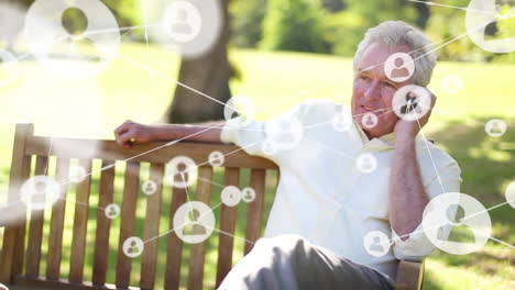 Animation-of-connected-icons,-senior-caucasian-man-sitting-on-bench-and-talking-on-cellphone-at-park