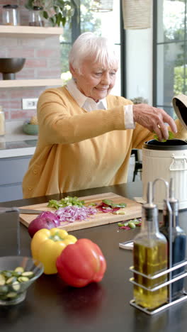 Vídeo-Vertical-De-Una-Mujer-Caucásica-Mayor-Limpiando-Cáscaras-De-Verduras-En-La-Cocina-De-Casa,-Cámara-Lenta