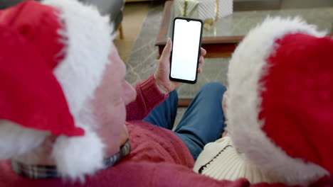 Senior-caucasian-couple-in-santa-hats-with-smartphone-with-copy-space-at-christmas,-slow-motion