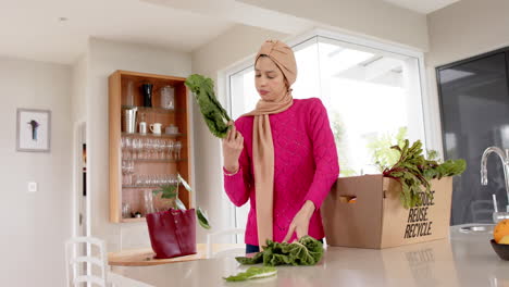Mujer-Birracial-En-Hijab-Con-Compras-En-La-Cocina-De-Casa-Con-Espacio-Para-Copiar,-Cámara-Lenta