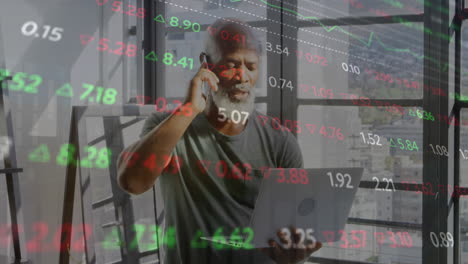 Animation-of-trading-board,-african-american-man-standing-with-laptop-and-talking-on-cellphone