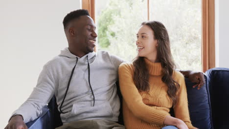 Happy-diverse-couple-sitting-on-sofa-talking-and-smiling-in-home,copy-space