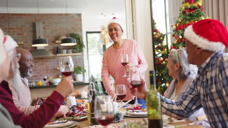 Happy-diverse-senior-woman-standing-making-a-toast-to-friends-at-christmas-dinner,-slow-motion