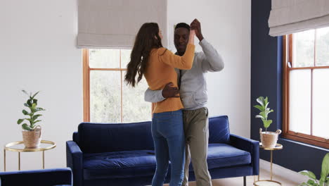 Happy-diverse-couple-dancing-and-smiling-in-sunny-living-room,copy-space
