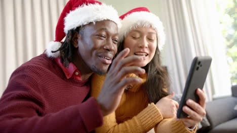 Happy-diverse-couple-having-christmas-video-call-on-smartphone,-waving-at-home,-slow-motion