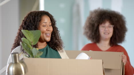Casual-biracial-businesswomen-carrying-boxes-moving-into-office,-slow-motion-with-copy-space