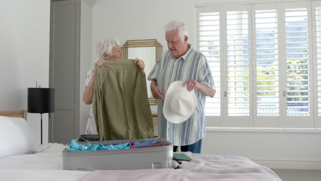 Senior-caucasian-couple-packing-suitcase-in-bedroom-at-home,-slow-motion
