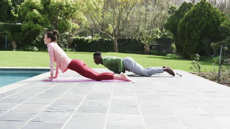 Happy-diverse-couple-exercising-yoga-in-sunny-garden,-slow-motion,-copy-space