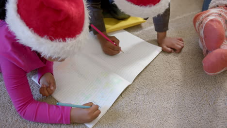 African-american-brother-and-sister-in-christmas-hats-drawing-on-floor-in-living-room,-slow-motion