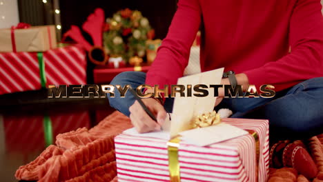 Animation-of-happy-holidays-text-over-caucasian-man-writing-christmas-cards-with-presents