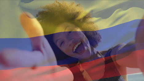 Animation-Einer-Kolumbianischen-Flagge,-Die-über-Einer-Frau-Mit-Gemischter-Abstammung-Weht-Und-Ein-Selfie-Video-Durch-Die-Kamera-Am-Strand-Macht