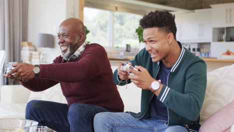 Aufgeregter-Afroamerikanischer-Vater-Und-Erwachsener-Sohn-Spielen-Zu-Hause-Videospiele-Mit-Gamepads,-Zeitlupe