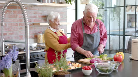 Glückliches-älteres-Kaukasisches-Paar-Mit-Schürzen,-Das-Zu-Hause-In-Der-Küche-Das-Abendessen-Kocht,-Zeitlupe