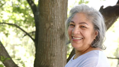Portrait-of-happy-senior-biracial-woman-with-grey-hair-in-sunny-nature,-copy-space,-slow-motion