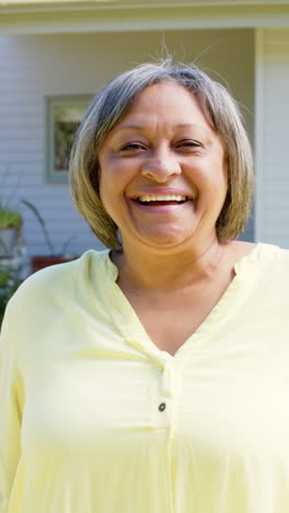 Vertical-video-of-portrait-of-happy-senior-biracial-woman-smiling-outside-house,-slow-motion