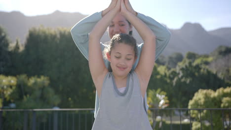 Happy-biracial-mother-and-daughter-practising-yoga-on-terrace-in-sunny-day,-slow-motion