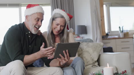 Middle-aged-caucasian-couple-in-santa-hats-on-tablet-video-chat-at-christmas-at-home,-slow-motion