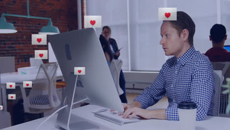 Animation-of-heart-shape-in-envelopes-over-biracial-man-working-on-desktop-in-office