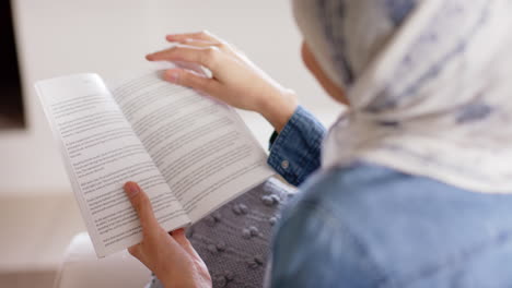 Happy-biracial-woman-in-hijab-reading-book-on-sofa-at-home-with-copy-space,-slow-motion