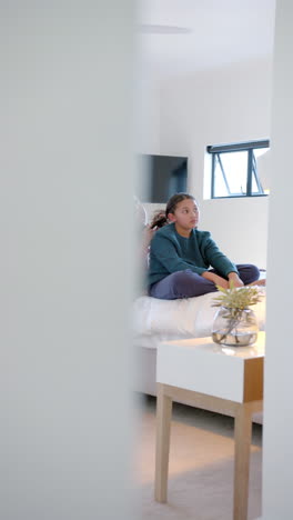 Vertical-video-of-happy-biracial-mother-with-daughter-and-taking-care-of-her-hair-in-sunny-bedroom