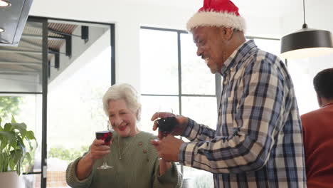 Happy-diverse-male-and-female-senior-friends-celebrating-christmas-with-wine-at-home,-slow-motion