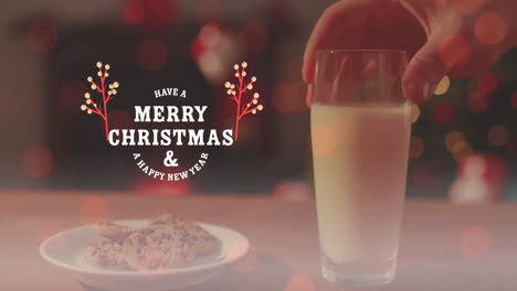 Animation-of-merry-christmas-and-a-happy-new-year-text,-cropped-hand-keeping-cookies-and-milk-glass