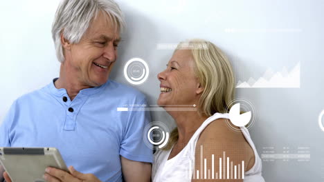 Animation-of-multiple-graphs-over-caucasian-senior-couple-laughing-while-relaxing-with-tablet-in-bed