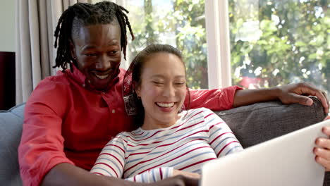 Happy-diverse-couple-relaxing-on-couch-using-laptop-in-living-room,-slow-motion