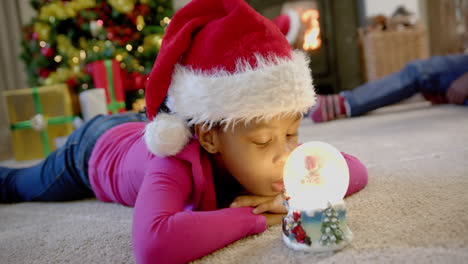 African-american-daughter-in-christmas-hat-with-glowing-snow-globe,-parents-behind,-slow-motion