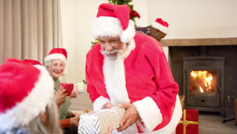 Fröhliche,-Abwechslungsreiche-Seniorenfreunde-Im-Weihnachtsmann-Outfit-Und-Weihnachtsmützen-Tauschen-Zu-Hause-Geschenke-Aus,-Zeitlupe