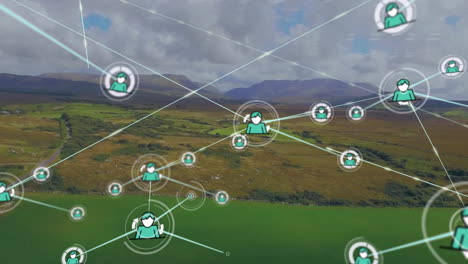Animation-of-connected-icons-over-aerial-view-of-green-land-against-mountains-and-cloudy-sky