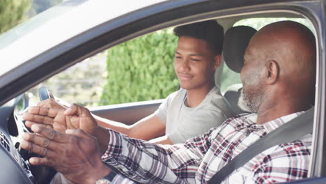 Happy-african-american-father-instructing-smiling-son-in-car-before-driving-lesson,-slow-motion