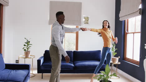 Happy-diverse-couple-dancing-and-smiling-in-sunny-living-room,copy-space