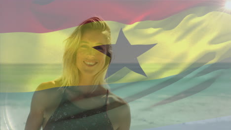 Animation-of-waving-flag-of-ghana-over-smiling-caucasian-woman-standing-against-sea-at-beach