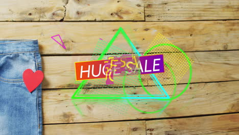 Animation-of-huge-sale-text-over-denim-trousers-on-wooden-background