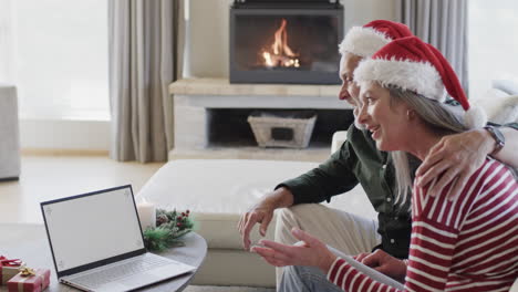 Caucasian-couple-in-santa-hats-with-laptop-with-blank-screen-at-christmas-at-home,-slow-motion