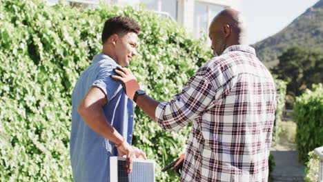 African-american-father-talking-to-adult-son-holding-solar-panel-in-sunny-garden,-slow-motion