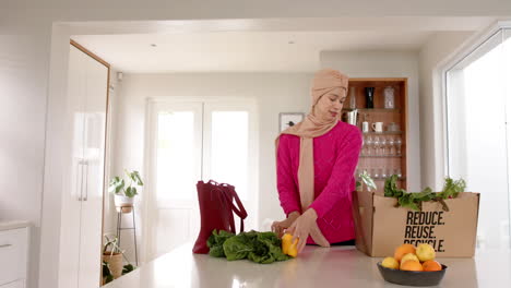 Biracial-woman-in-hijab-with-grocery-shopping-in-kitchen-at-home-with-copy-space,-slow-motion