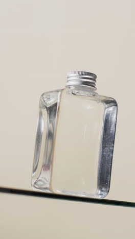 Vertical-video-of-beauty-product-bottle-on-glass-shelf-with-copy-space-on-white-background