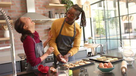 Happy-diverse-couple-in-aprons-decorating-christmas-cookies-in-kitchen,-copy-space,-slow-motion