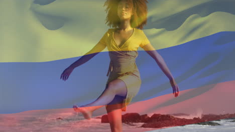 Animation-of-flag-of-colombia-waving-over-biracial-woman-walking-and-enjoying-breeze-at-beach