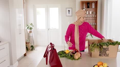 Mujer-Birracial-En-Hijab-Con-Compras-En-La-Cocina-De-Casa-Con-Espacio-Para-Copiar,-Cámara-Lenta