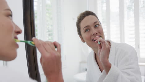 Biracial-woman-brushing-teeth-looking-in-mirror-in-bathroom,-slow-motion