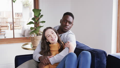 Happy-diverse-couple-sitting-on-sofa-laughing-and-embracing-in-home,copy-space